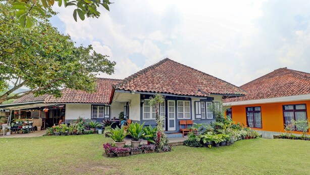 A two-story building with a tiled roof, a covered porch, and a well-maintained lawn with various potted plants. - OYO Homes 90850 Cibeunying Eco Tourism Homestay Cibodas Maribaya 2 (Lembang)