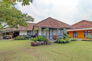 A two-story building with a tiled roof, a covered porch, and a well-maintained lawn with various potted plants. - OYO Homes 90850 Cibeunying Eco Tourism Homestay Cibodas Maribaya 2 (Lembang)