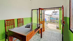 A room with a glass-top table, wooden chairs, a green wall, and a door leading outside. - OYO Homes 90850 Cibeunying Eco Tourism Homestay Cibodas Maribaya 2 (Lembang)