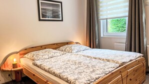 Una cama doble con ropa de cama floral, una lámpara de noche, un cuadro en la pared y una ventana con cortinas.