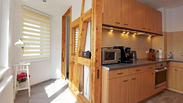Una cocina moderna con armarios de madera, microondas, cafetera y una pequeña mesa con lámpara y flores.