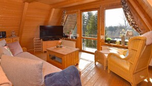 Een gezellig houten interieur van een blokhut met een bank, een televisie, een kleine tafel en rieten stoelen.