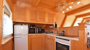 Een kleine keuken met houten kastjes, een koelkast, een magnetron, een koffiezetapparaat en een fornuis.