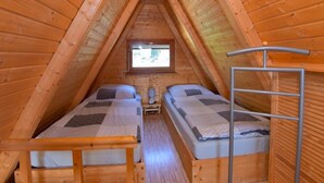 Een kleine kamer met houten afwerking, in zolderstijl, met twee bedden, een raam en een ladder.