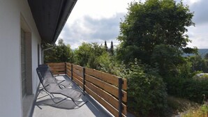 A balcony with a wooden bench and a chair, overlooking a lush garden and trees. - Vacation home Selma by Interhome (Suhl)