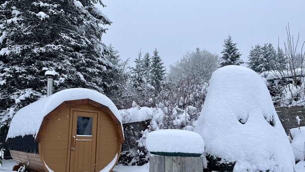 A snow-covered wooden cabin with a door and a window, surrounded by trees and a snow-covered bush. - Vacation home Selma by Interhome (Suhl)