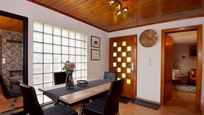 A dining area with a wooden table, black chairs, a vase with flowers, and a large window with a view. - Vacation home Selma by Interhome (Suhl)