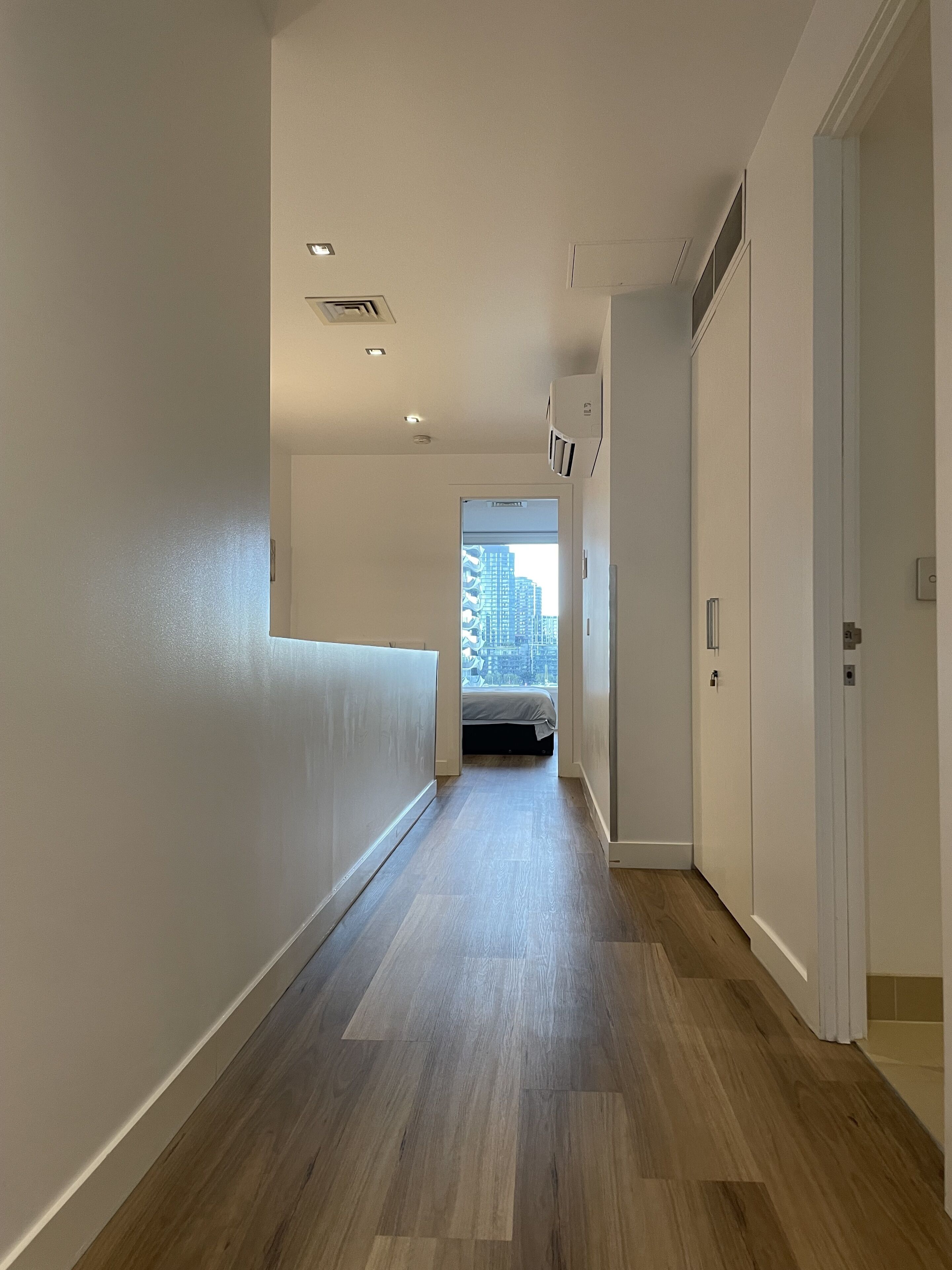 Un couloir doté d’un plancher en bois, de murs blancs et d’une porte donnant sur une pièce avec vue sur la ville.