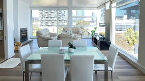 A modern living room with a glass dining table, white chairs, a fireplace, and large windows offering city views. - Luxury Penthouse Above the Shopping Town (Docklands)