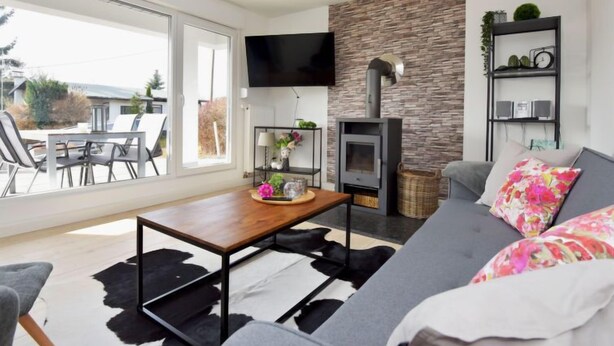 A modern living room with a stone wall, a fireplace, a flat-screen TV, a sofa, and a dining area with a table and chairs.