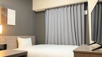 A hotel room with a bed, a desk, a chair, a TV, and a window with curtains.