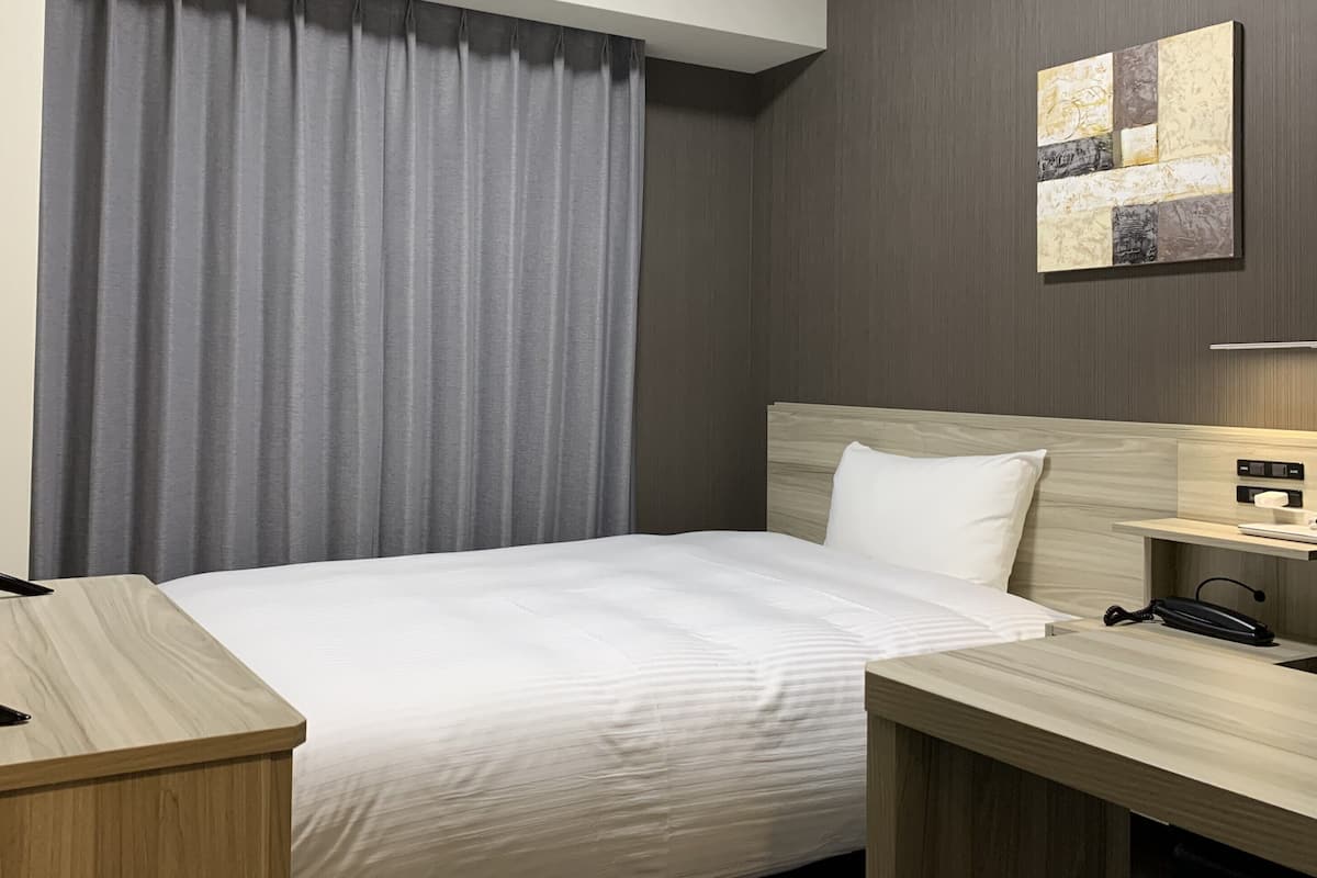 A hotel room with a bed, a desk, a TV, a lamp, and a painting on the wall.