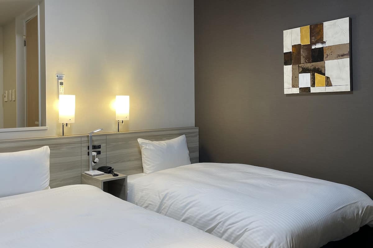 A hotel room with two beds, a nightstand, a lamp, a telephone, a flat-screen TV, and a wall-mounted artwork.