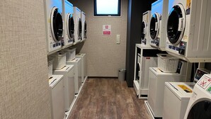 A laundry facility with multiple washing machines and dryers, a wooden floor, and a small window. - Hotel Route Inn Shikoku Chuo - Mishimaka (Shikokuchuo)