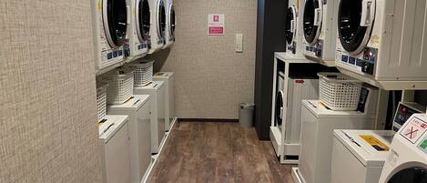A laundry facility with multiple washing machines and dryers, a wooden floor, and a small window.