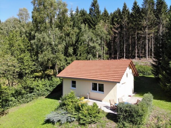 Ein kleines, eingeschossiges Haus mit rotem Ziegeldach, umgeben von dichtem Wald.