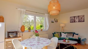 A cozy living room with a green sofa, a round table with chairs, a small kitchen area with a microwave, and a large window with curtains. - Vacation home Konrad by Interhome (Suhl)