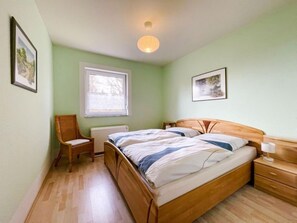 Ein Schlafzimmer mit einem hölzernen Bett, einem Sessel, einem Nachttisch und einem Fenster mit Blick.