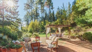 An outdoor patio with wicker furniture, a pergola, and a stone wall. - Villa Birdsong, among the Woods in Camaiore (Camaiore)