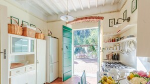 A kitchen with white cabinets, a refrigerator, and a dining area with a table and chairs. - Villa Birdsong, among the Woods in Camaiore (Camaiore)