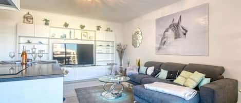 A modern living room with a grey sofa, a glass coffee table, and a large painting on the wall.