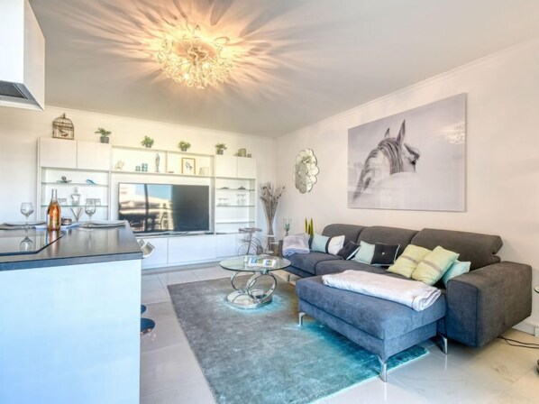 A modern living room with a grey sofa, a glass coffee table, and a large painting on the wall.
