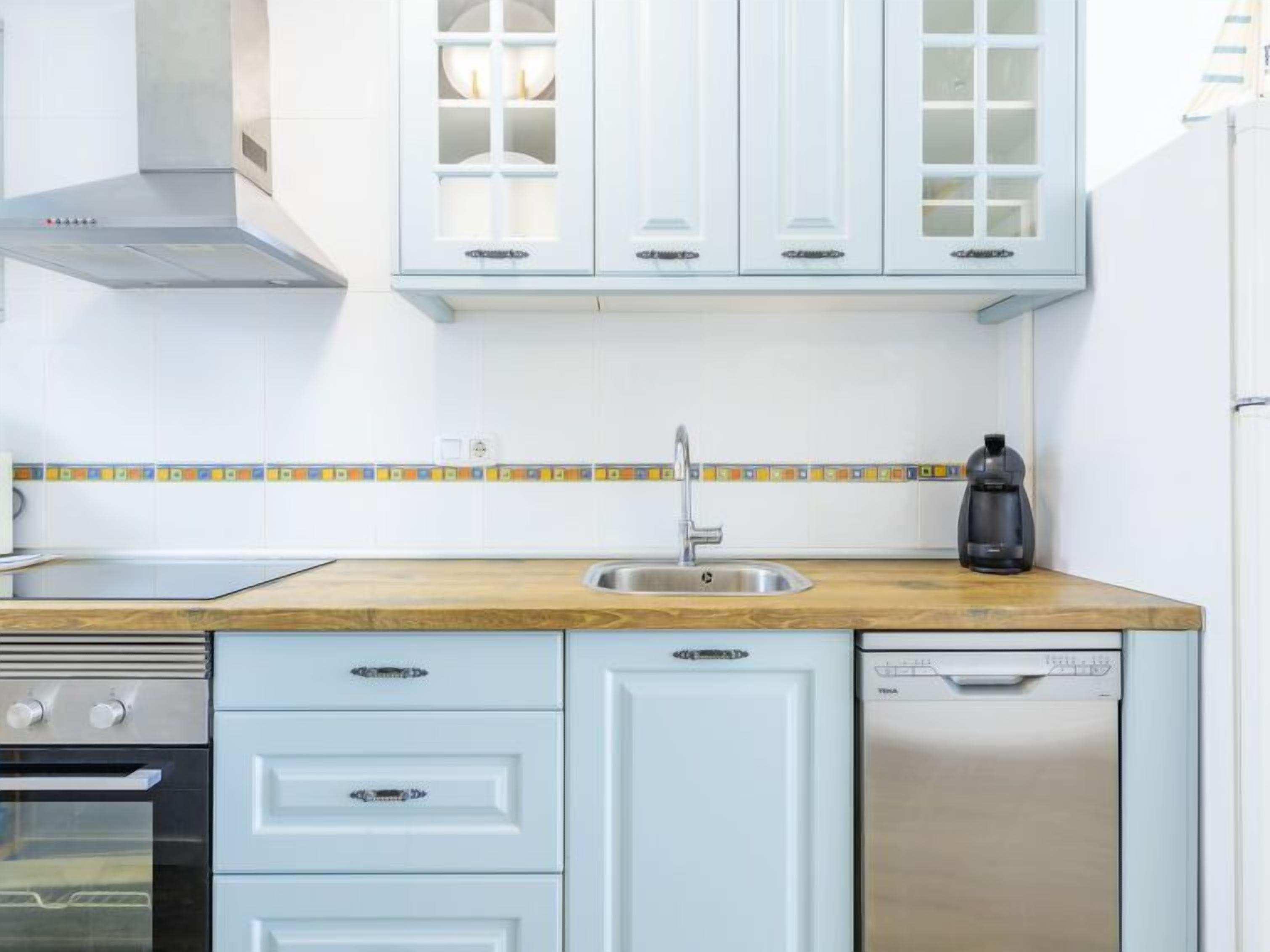 Een keuken met witte kastjes, een houten aanrecht, een roestvrijstalen spoelbak, een koffiezetapparaat, een oven en een vaatwasser.
