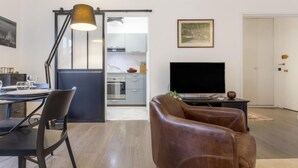 A modern living room with a leather sofa, a dining table with chairs, a TV, and a kitchen in the background. - Jean Mermoz by Interhome (Deauville-Trouville)