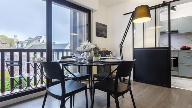 A modern kitchen with a large window, a dining area with two black chairs, and a black floor lamp. - Jean Mermoz by Interhome (Deauville-Trouville)
