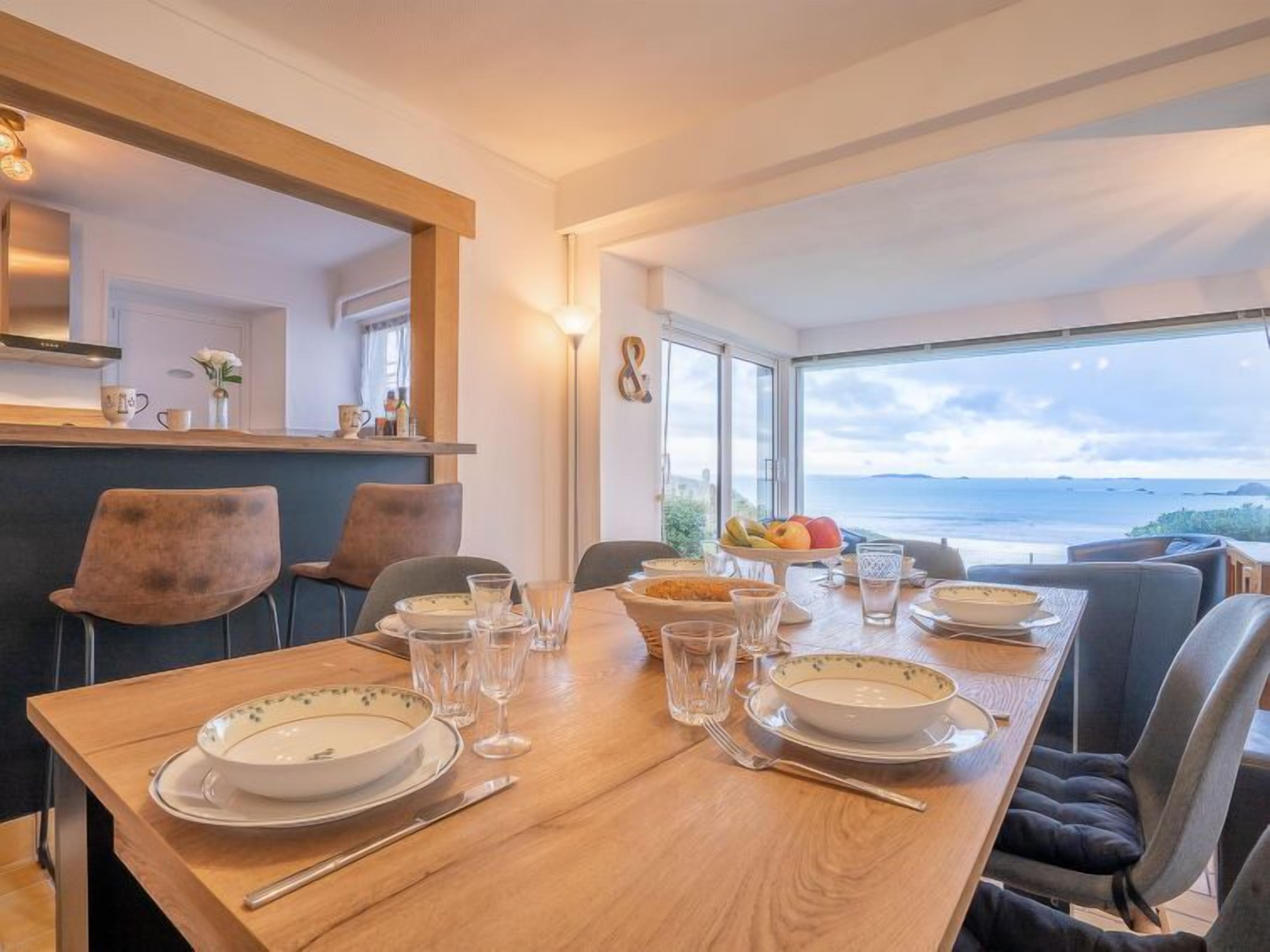 Un coin repas avec une table dressée pour quatre personnes, une vue sur la mer et un aménagement intérieur moderne.