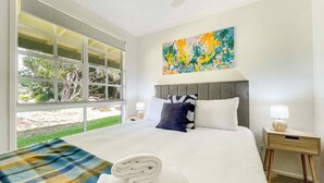 A hotel room with a large bed, a window with a view of greenery, a painting on the wall, and a nightstand with a lamp. - Broke in the Vines - 6 bedroom farmhouse on working vineyard (Broke)