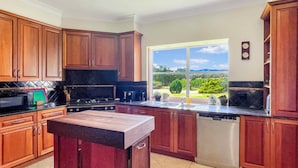 A kitchen with wooden cabinets, a black countertop, a stove, and a view of a garden through a large window. - Broke in the Vines - 6 bedroom farmhouse on working vineyard (Broke)