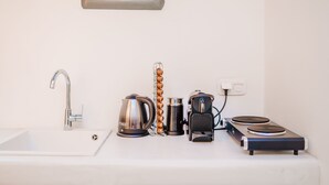 Un baño moderno con un lavabo blanco, un grifo plateado, un hervidor, una cafetera y una hornilla eléctrica portátil.