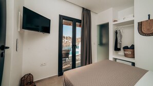 Habitación de hotel con cama, televisor, vista a una piscina y armario con ropa colgada y cestas.