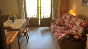 A cozy room with a wooden sofa, a small table with a vase of flowers, and a lamp. - Studio Combloux Avec Balcon, 1 Pièce, 4 Personnes, Près des Pistes (Combloux)