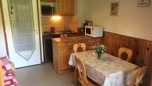 A compact kitchen with wooden cabinets, a microwave, and a dining table with chairs. - Studio Combloux Avec Balcon, 1 Pièce, 4 Personnes, Près des Pistes (Combloux)