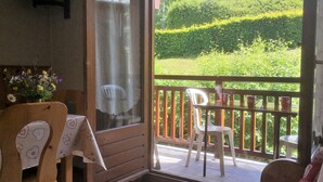A room with a wooden chair, a table with a cloth, and a window overlooking a garden. - Studio Combloux Avec Balcon, 1 Pièce, 4 Personnes, Près des Pistes (Combloux)