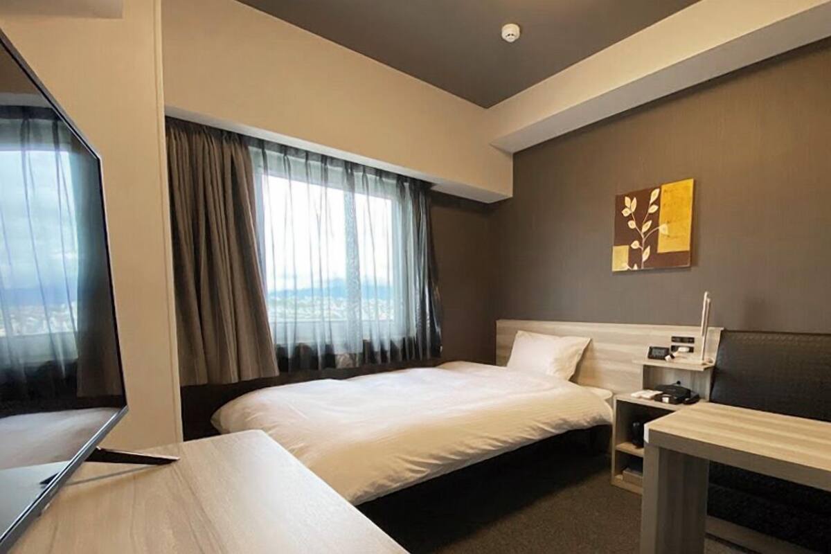 Habitación de hotel con cama, escritorio, silla, mesita de noche y televisor montado en la pared.