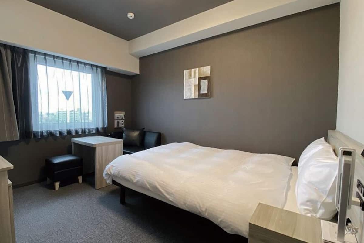 Habitación de hotel con cama, escritorio, silla y ventana con cortinas.