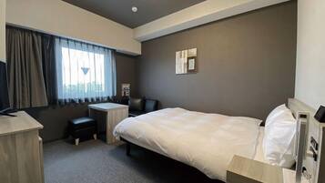 A hotel room with a bed, a desk, a chair, and a window with curtains.