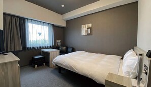 Habitación de hotel con cama, escritorio, silla y ventana con cortinas.