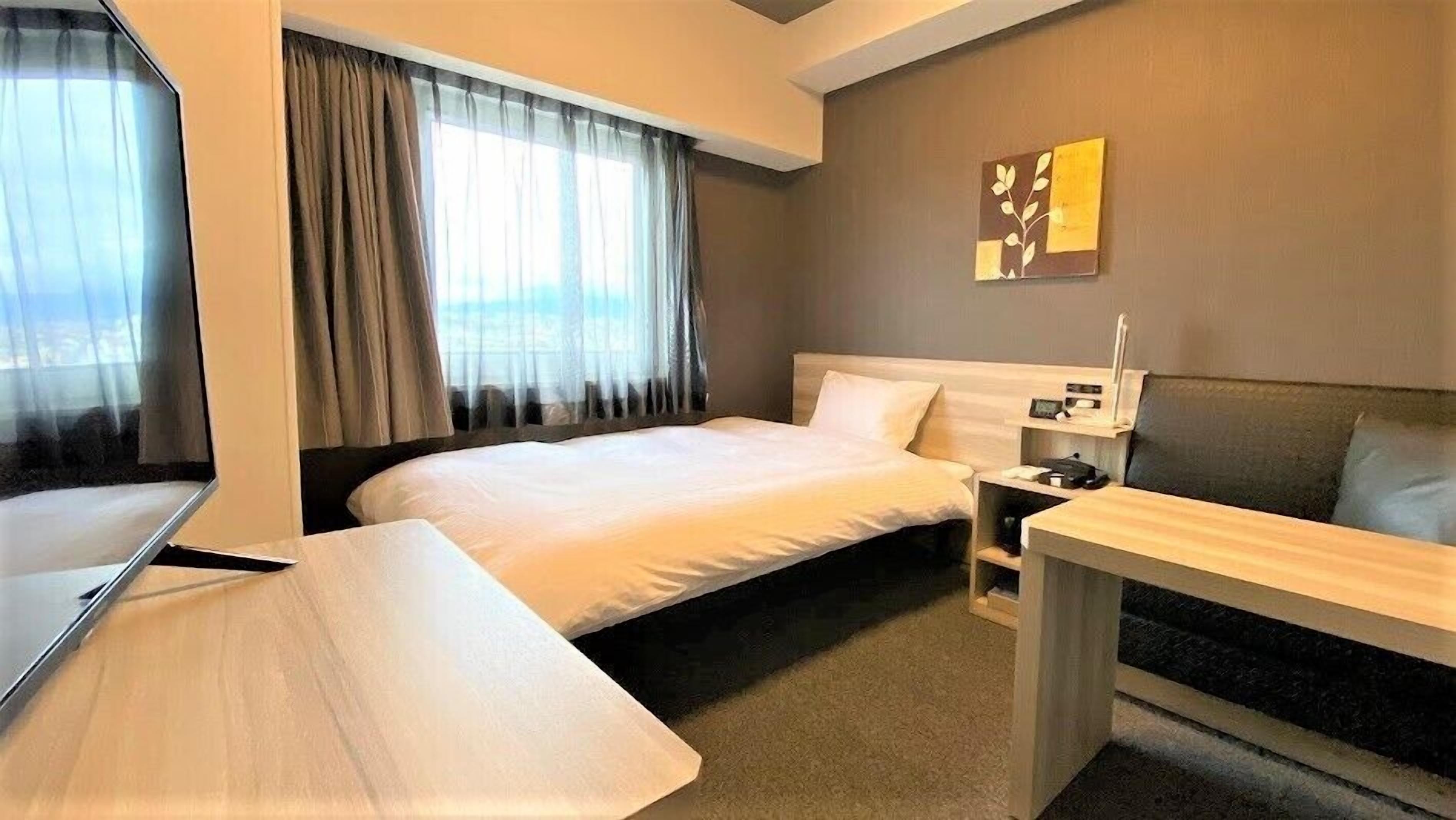 Une chambre d’hôtel avec un lit, un bureau, une chaise, une télévision et une fenêtre avec des rideaux.