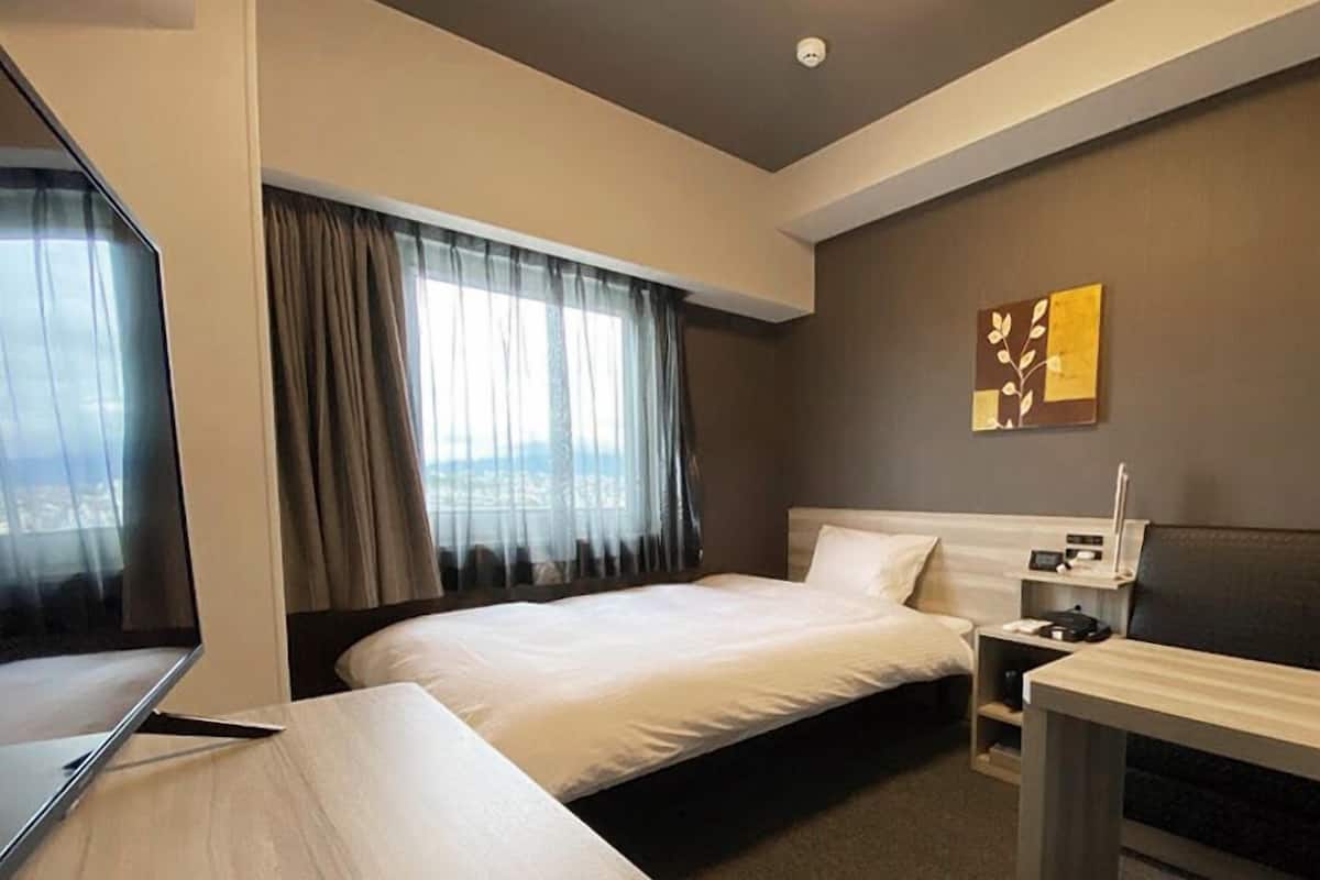 Une chambre d’hôtel équipée d’un lit, d’un bureau, d’une chaise, d’une table de chevet et d’un téléviseur fixé au mur.