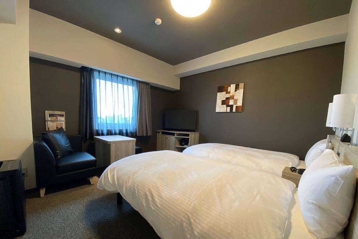 Habitación de hotel con una cama grande, un escritorio, una silla, un televisor y una ventana con cortinas.