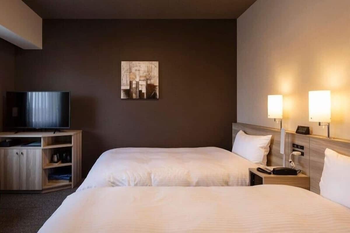 Una habitación de hotel con dos camas, un televisor, un cuadro en la pared y lámparas de noche.