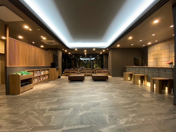 A hotel lobby with a modern design, featuring a central seating area, a reception desk, and a large window providing natural light. - Hotel Route Inn Osaka Izumifuchu (Izumi)