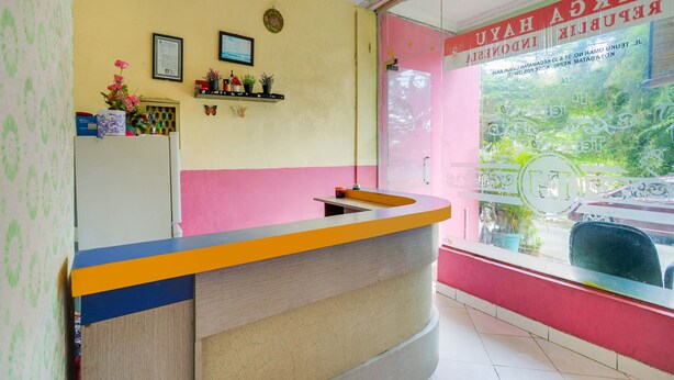 A reception desk with a pink and yellow wall, a framed certificate, and a butterfly decoration. - Hotel O Emes Jaya HomestayNearSamsung Electronic Indonesia PT (Batam)