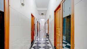 Un couloir d’hôtel aux murs recouverts de carreaux blancs, au sol à motifs à carreaux et aux portes en bois.