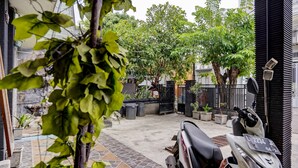 Une cour intérieure où est garé un scooter Honda, entourée de plantes en pot et dotée d’un sol carrelé en pierre.