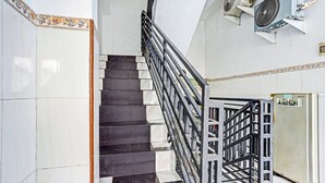 Un escalier avec une rampe en métal, des carreaux blancs et foncés, et des unités de climatisation fixées au mur.